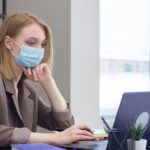 The image depicts a modern office setting where employees are wearing face masks while working together. This visual represents the adaptation of workplaces during the COVID-19 pandemic, highlighting the importance of safety protocols like mask-wearing in maintaining business operations. It reflects the shift towards health-conscious work environments that became crucial during the pandemic and reinforces the theme of adapting to new norms in industries like debt collection.