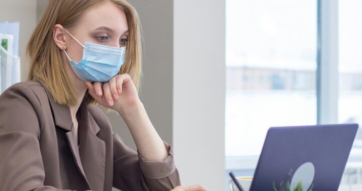 The image depicts a modern office setting where employees are wearing face masks while working together. This visual represents the adaptation of workplaces during the COVID-19 pandemic, highlighting the importance of safety protocols like mask-wearing in maintaining business operations. It reflects the shift towards health-conscious work environments that became crucial during the pandemic and reinforces the theme of adapting to new norms in industries like debt collection.